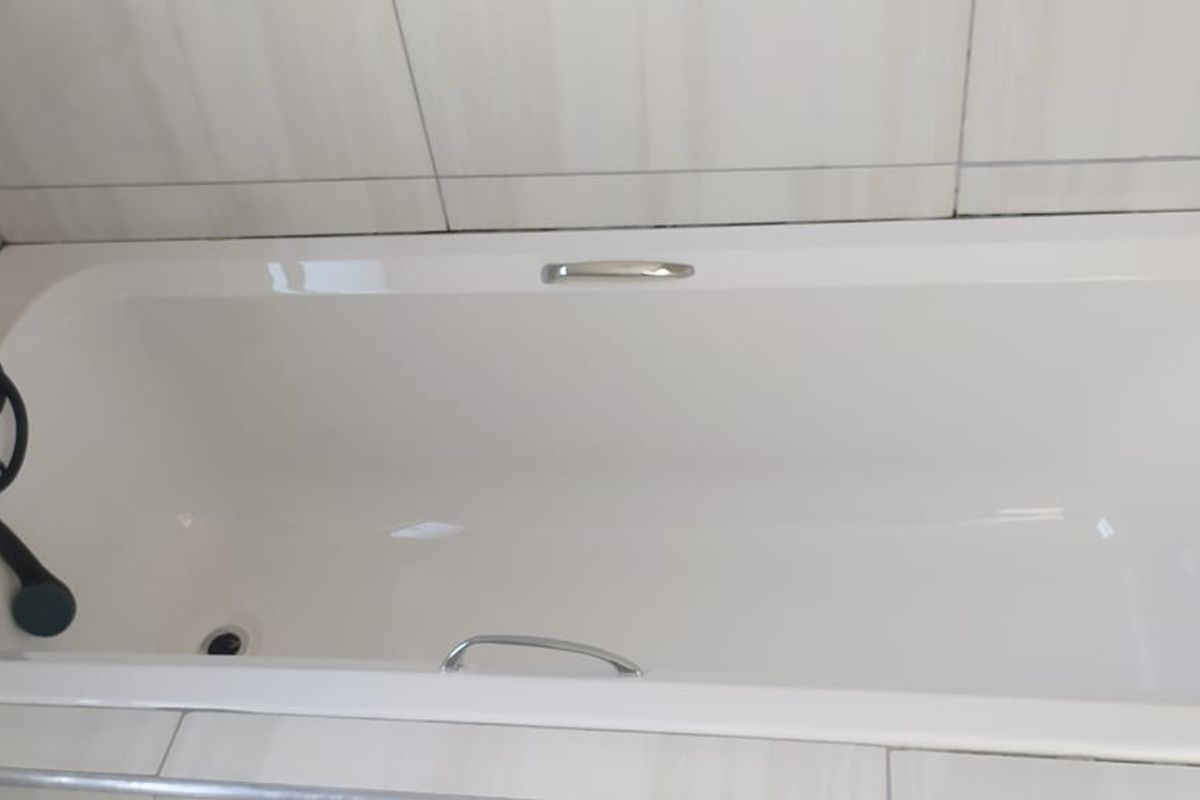 A clean, modern bathroom featuring a white built-in bathtub with contemporary matte black fixtures and tiled wall surrounds.