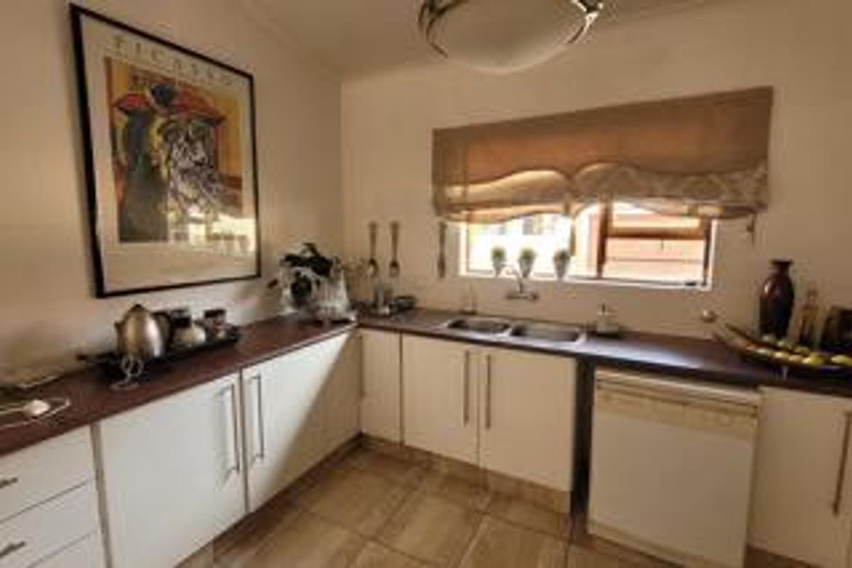 A functional kitchen featuring white cabinetry, dark countertops, a double basin sink, and an integrated dishwasher.