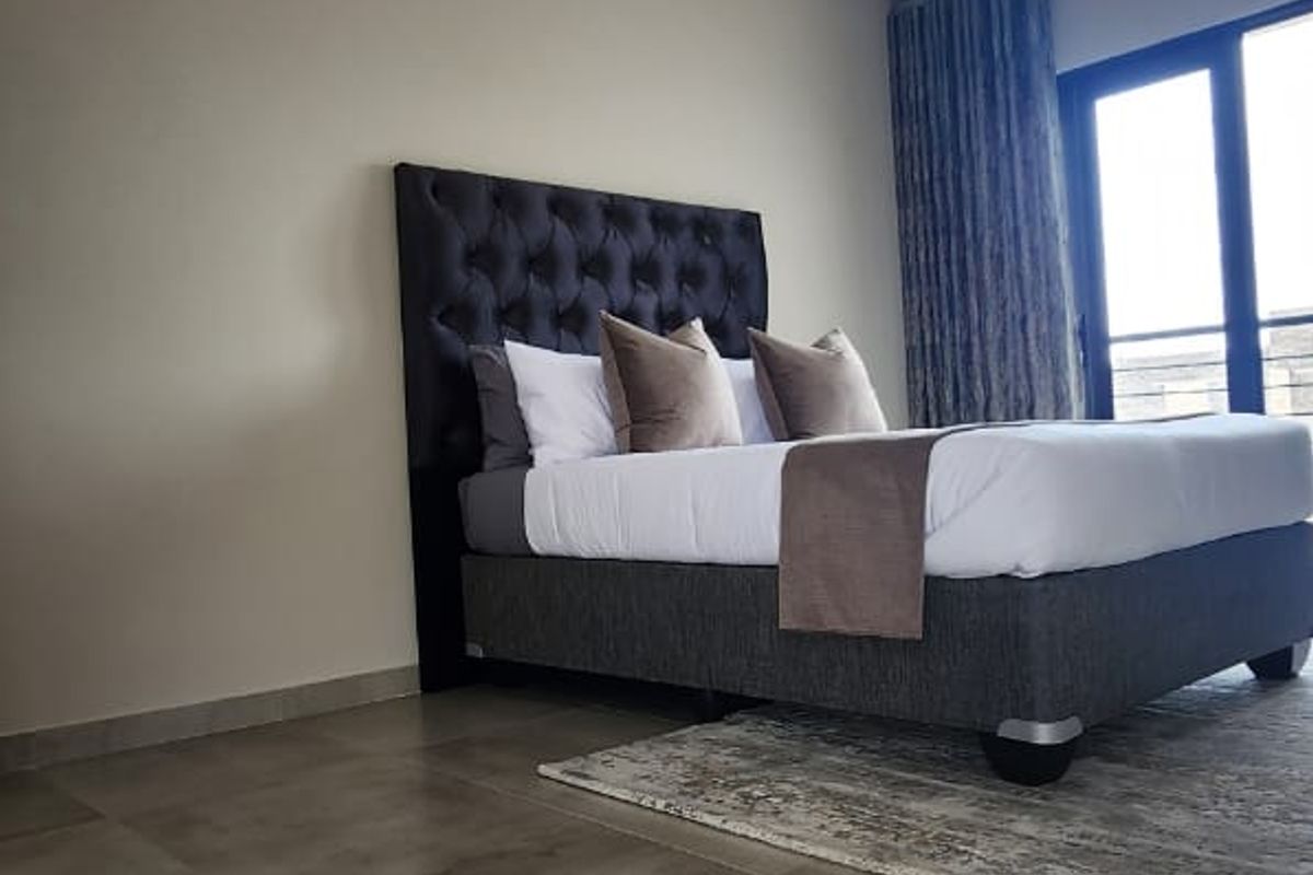 A modern bedroom featuring large format floor tiles, a tongue-and-groove ceiling, and glass sliding doors leading to an outdoor area.