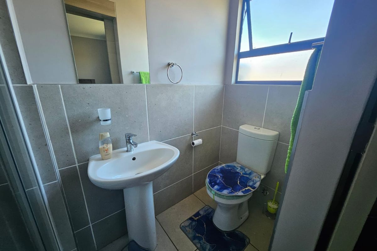 A compact bathroom featuring a pedestal basin, a wall-mounted mirror, and a standard toilet with tiled walls and flooring.