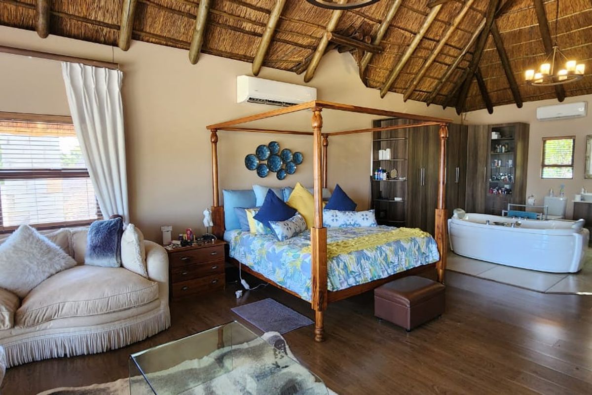 Spacious open-plan bedroom suite featuring a high thatched roof, exposed timber beams, integrated bathroom area with soaking tub, and split-system air conditioning.