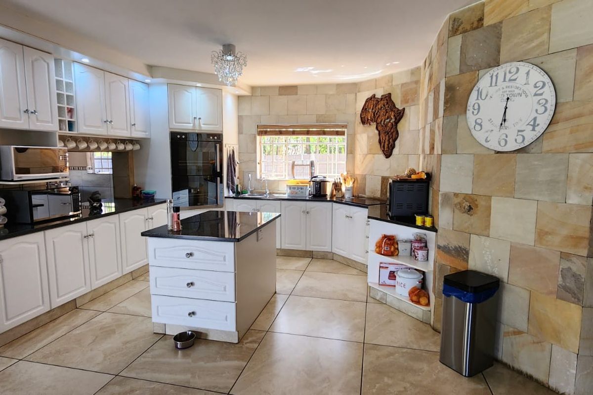 Spacious kitchen featuring white cabinetry, granite countertops, a central island, and a distinctive natural stone feature wall.