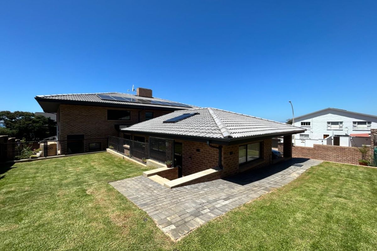Rear view of the property featuring a brick facade, tiled roof with solar panels, paved patio area, and a well-maintained lawn.