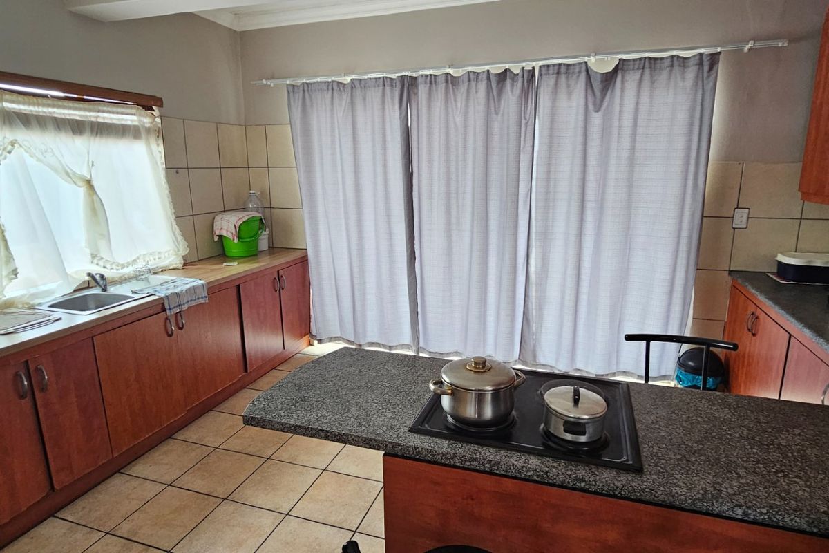 A functional kitchen featuring wood-look cabinetry, granite countertops, a built-in electric hob, and tiled flooring, offering a practical layout for daily meal preparation.