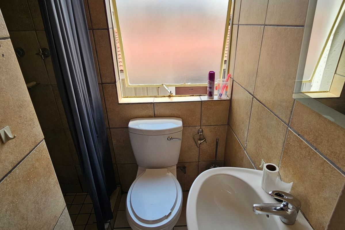 Compact bathroom featuring a pedestal basin, toilet, and shower area with tiled finishes and a frosted window for natural light.