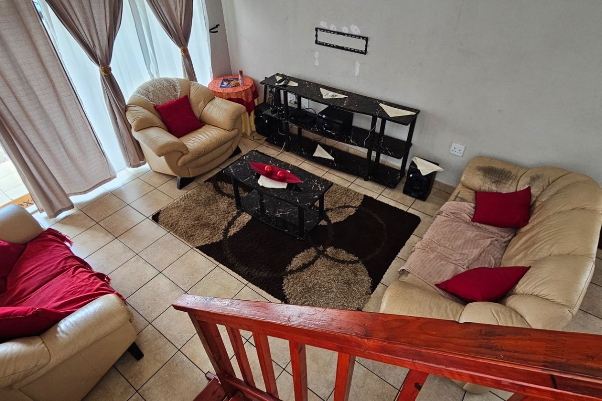 A living room featuring ceramic floor tiles, a sliding glass door providing natural light, and a wooden staircase railing overlooking the space.
