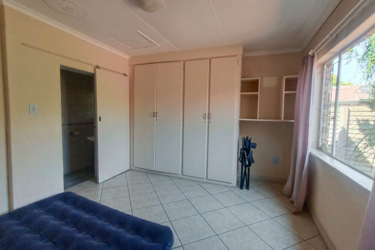 A bedroom featuring built-in cupboards, tiled flooring, and an en-suite bathroom access point, offering a functional layout with natural light.