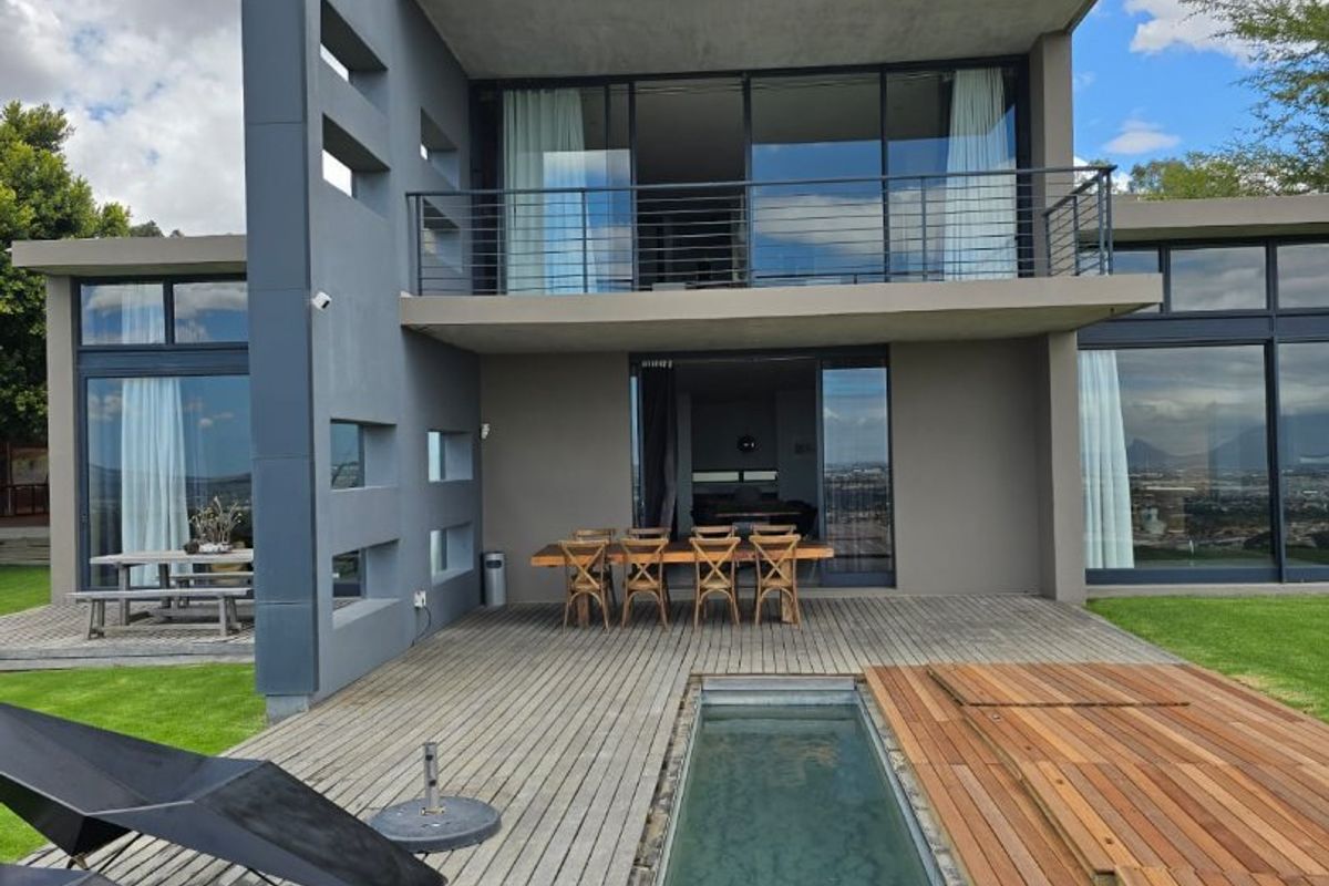 Modern two-story farm residence featuring a sleek rear facade, expansive glass sliding doors, a balcony, and a linear lap pool set into timber decking.