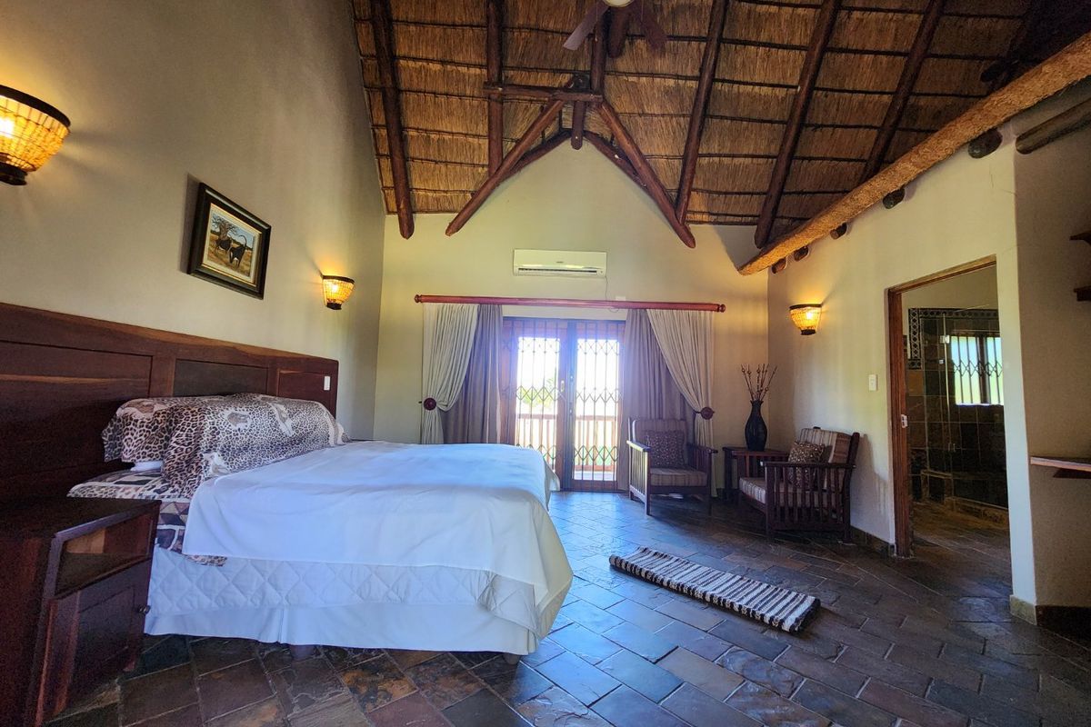 Spacious bedroom featuring a high vaulted thatched ceiling, exposed timber beams, slate tile flooring, and direct access to an outdoor area.