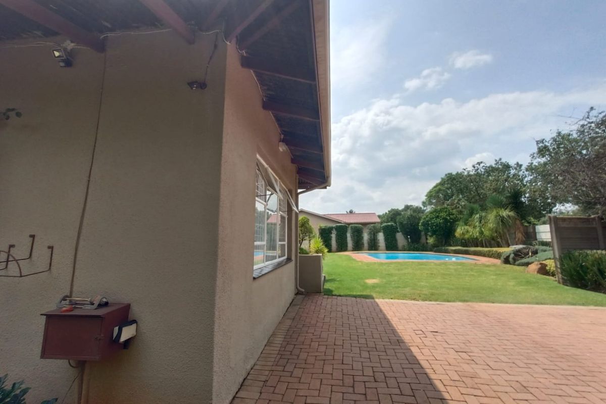 A rear exterior view featuring a paved patio area, a well-maintained lawn, and a swimming pool set within a private garden.