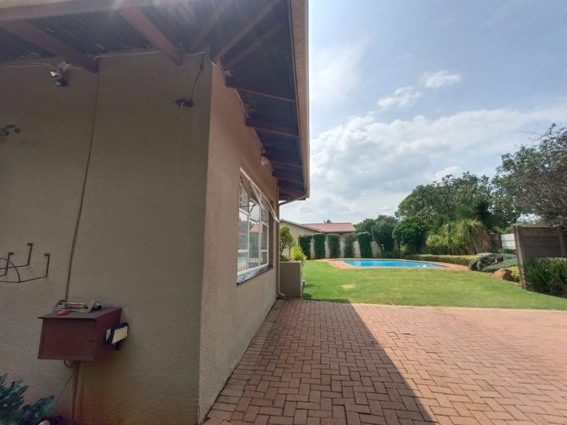 A rear exterior view featuring a paved patio area, a well-maintained lawn, and a swimming pool set within a private garden.
