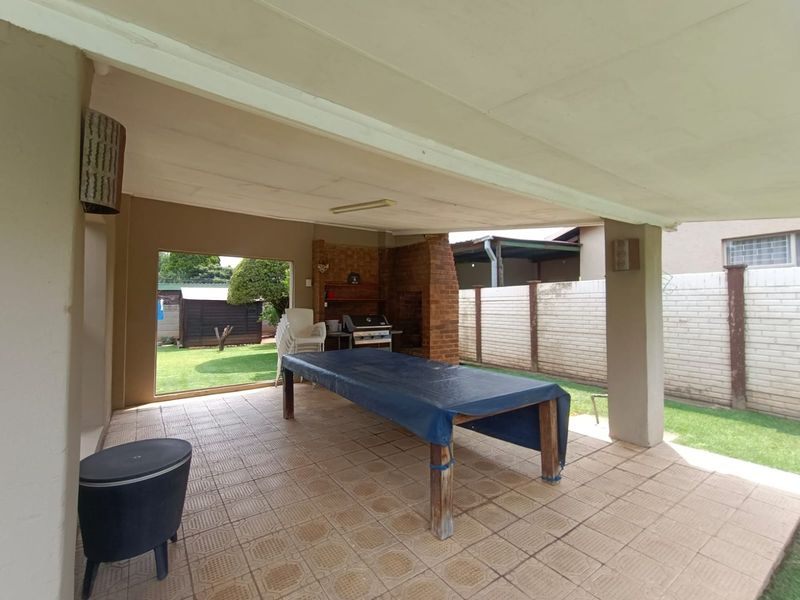 A covered outdoor patio featuring a built-in brick braai, tiled flooring, and direct access to the rear garden area.