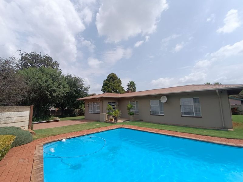 Rear view of the house featuring a swimming pool, brick paved surround, and a well-maintained lawn area.