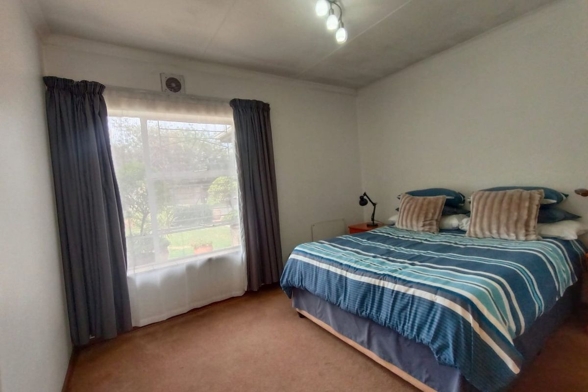 A bedroom featuring carpeted flooring, a wall-mounted extractor fan, and a ceiling light fixture, offering a functional space with potential for cosmetic updates.