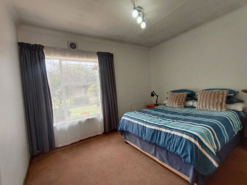 A bedroom featuring carpeted flooring, a wall-mounted extractor fan, and a ceiling light fixture, offering a functional space with potential for cosmetic updates.