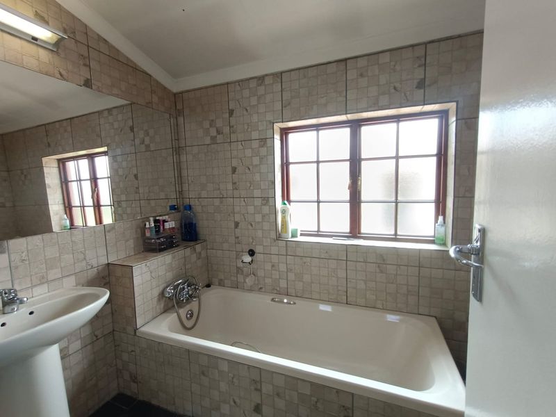 A functional bathroom featuring a pedestal basin, a built-in bathtub with chrome fixtures, and neutral tiled walls with a large mirror.