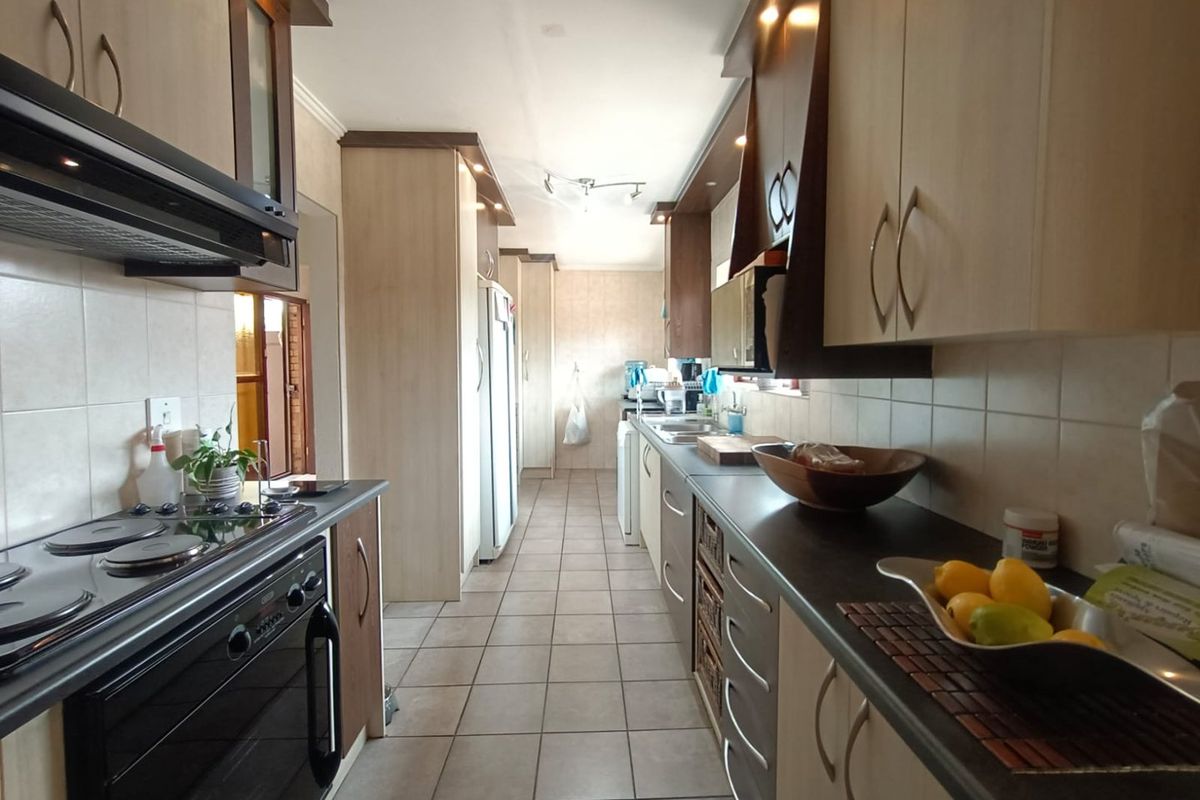 A functional galley-style kitchen featuring built-in cabinetry, an electric hob with extractor fan, tiled flooring, and a double sink with tiled backsplash.