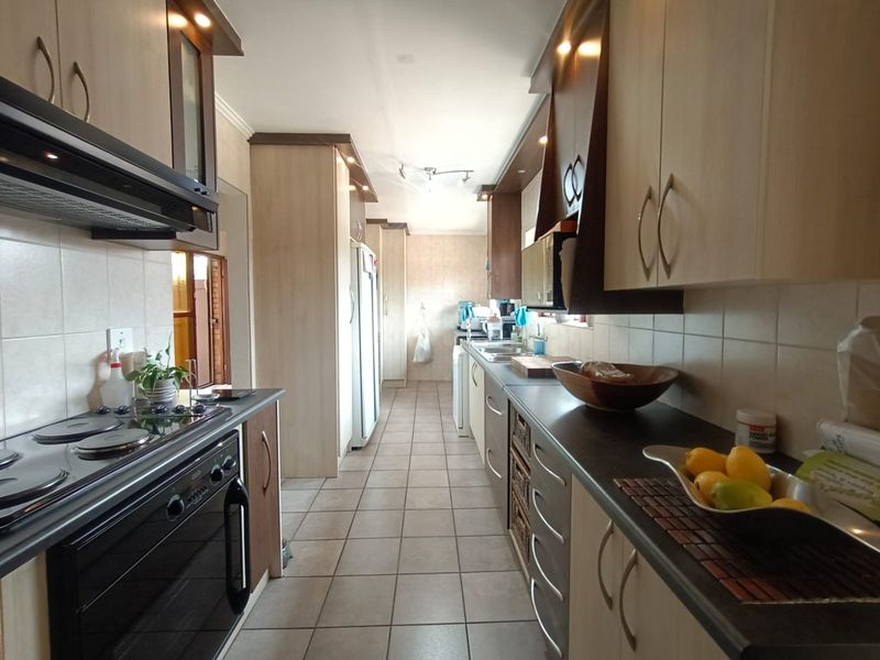 A functional galley-style kitchen featuring built-in cabinetry, an electric hob with extractor fan, tiled flooring, and a double sink with tiled backsplash.
