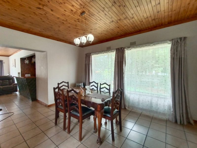 A dining room featuring a warm timber tongue and groove ceiling, ceramic tiled flooring, and large windows that provide ample natural light.