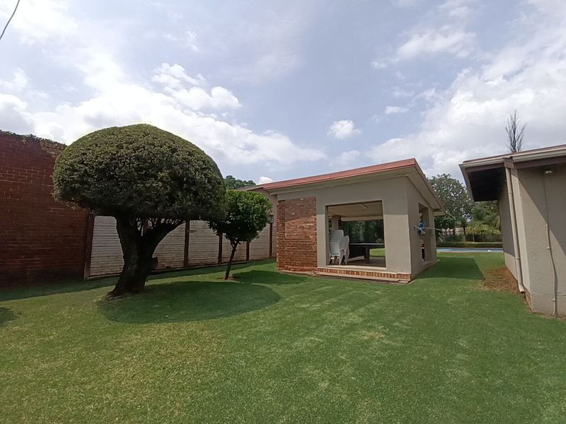 A spacious backyard featuring a well-maintained lawn, mature trees, and a covered patio area suitable for outdoor entertaining.