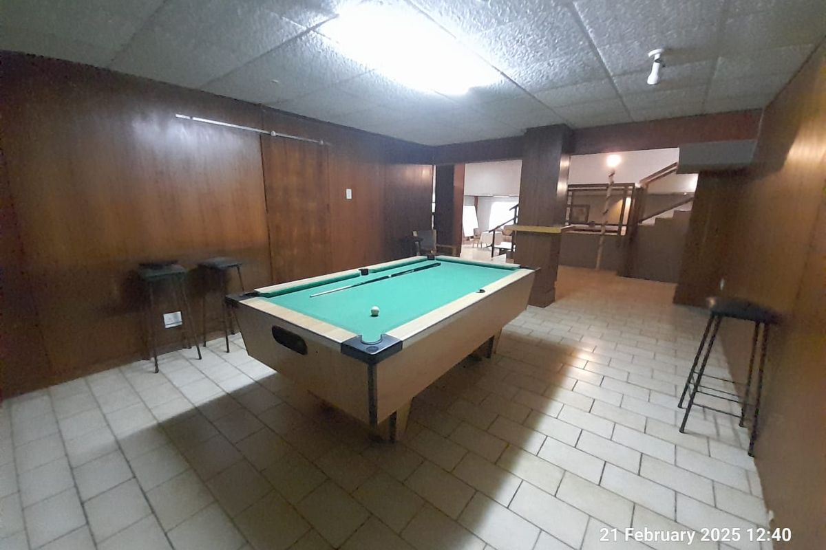 A spacious recreation room featuring wood-paneled walls, tiled flooring, and a drop ceiling, currently set up as a games area.