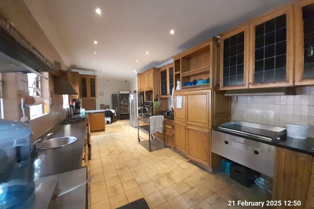 Spacious commercial-style kitchen featuring extensive wooden cabinetry, tiled flooring, integrated stainless steel cooking equipment, and recessed ceiling lighting.