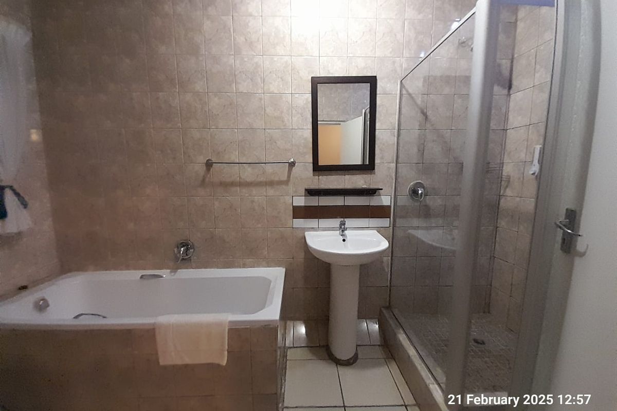 A functional bathroom featuring a built-in bathtub, a separate glass-enclosed shower, and a pedestal basin with wall-mounted mirror.