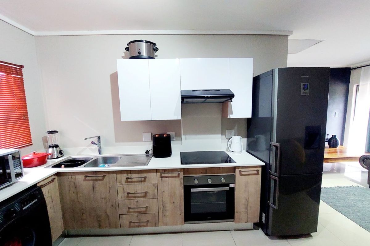 Modern kitchen featuring wood-finish lower cabinetry, white upper cabinets, integrated electric hob, oven, extractor fan, and tiled flooring.