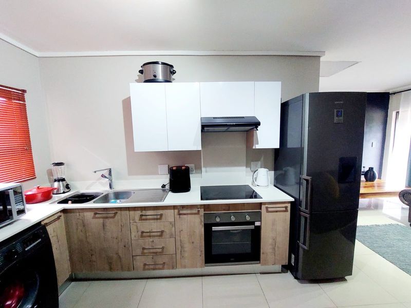 Modern kitchen featuring wood-finish lower cabinetry, white upper cabinets, integrated electric hob, oven, extractor fan, and tiled flooring.