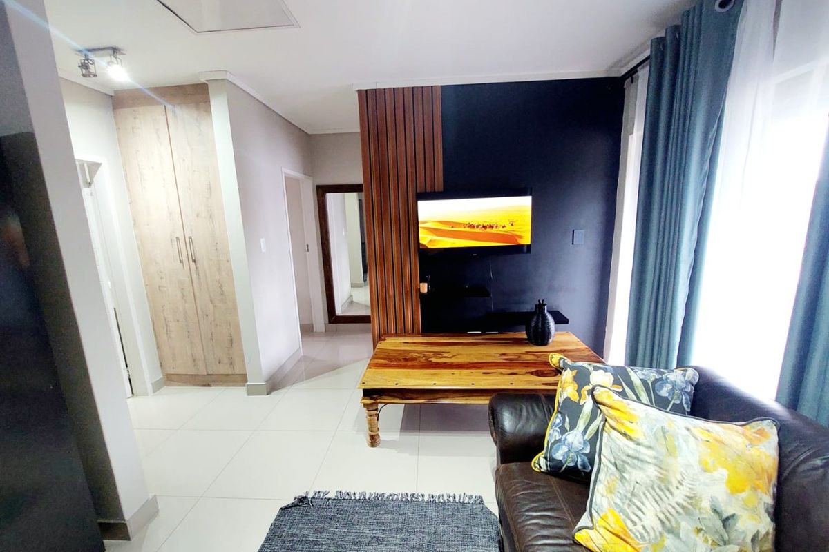 A modern living room featuring tiled flooring, built-in cabinetry, and a decorative slatted wood feature wall with a mounted television.