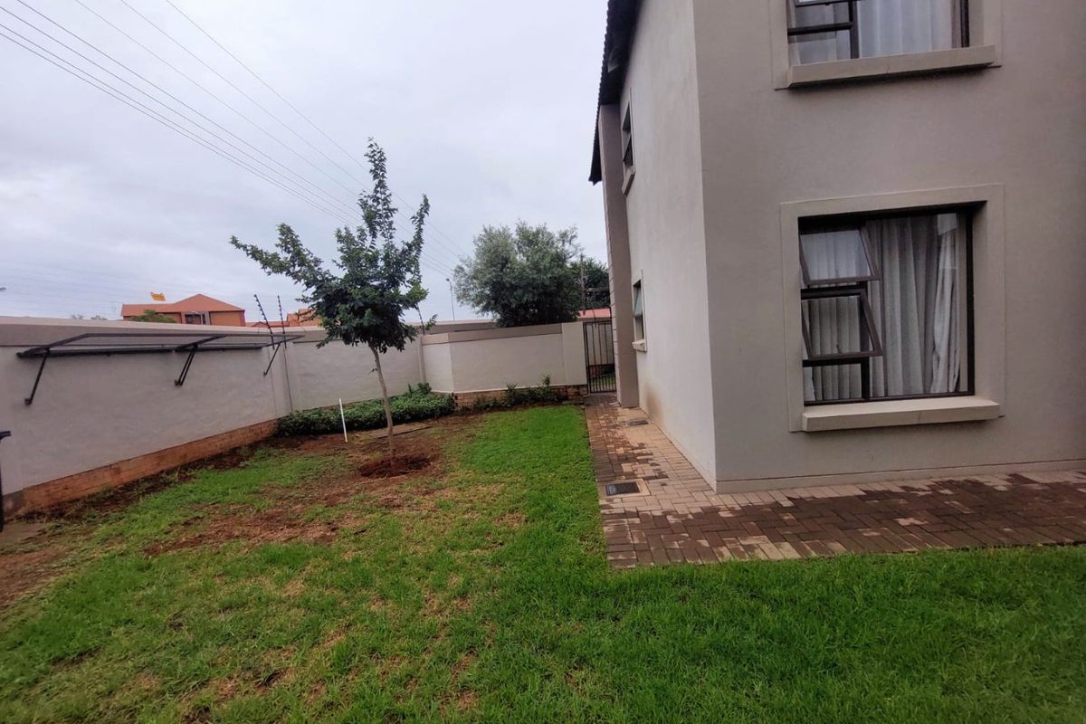 A rear garden area featuring a paved walkway, perimeter wall with electric fencing, and a wall-mounted washing line.
