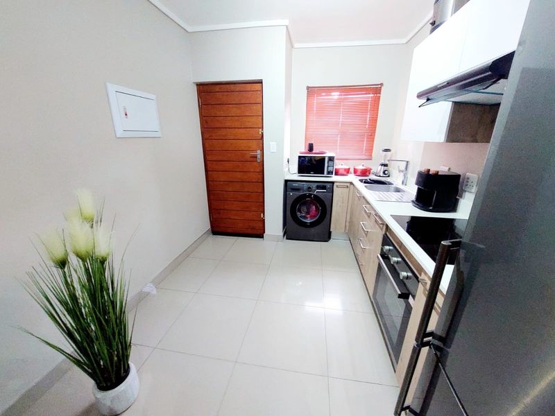 A modern, well-maintained kitchen featuring built-in cabinetry, an electric hob, oven, extractor fan, and tiled flooring with a wooden exterior door.