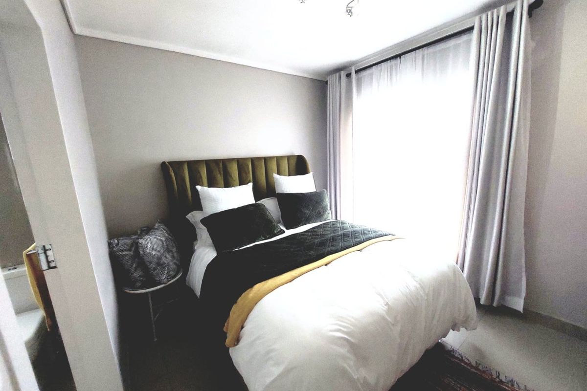 A well-lit bedroom featuring neutral wall tones, large window with curtain rails, and tiled flooring.