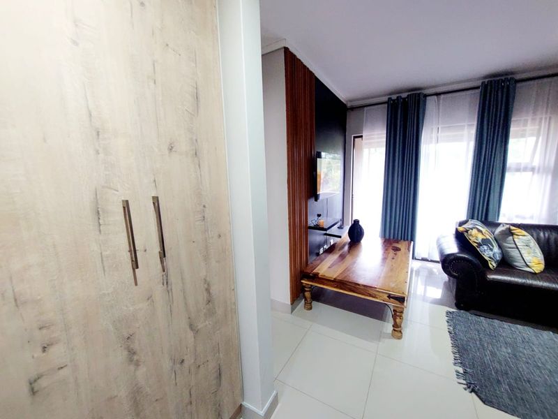 A modern living room featuring light wood-look built-in cupboards, tiled flooring, and a feature wall with direct access to an outdoor area.