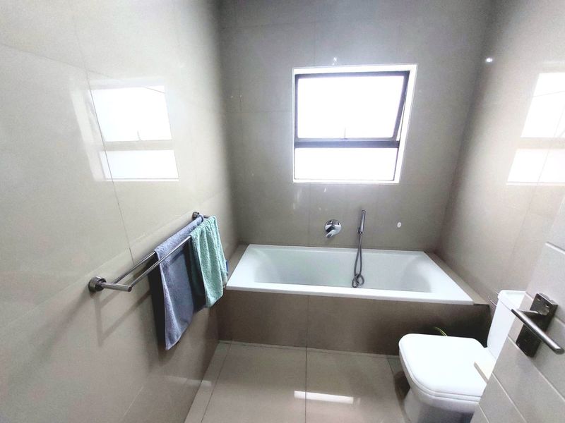 A modern bathroom featuring a built-in bathtub with a handheld shower attachment, tiled walls, and a standard toilet.