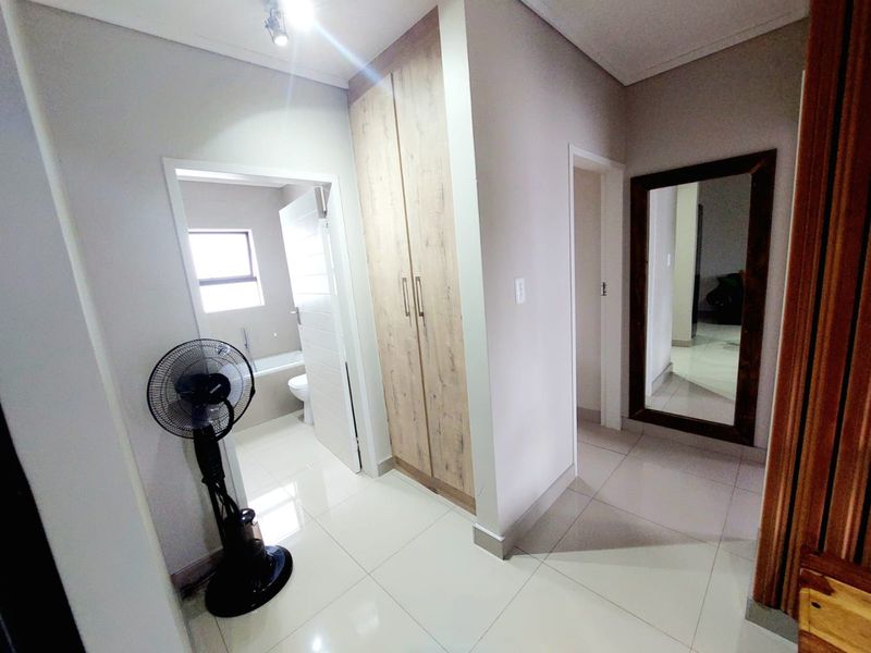A clean, well-maintained hallway featuring neutral tiled flooring, built-in wooden cupboards, and direct access to an adjacent bathroom.