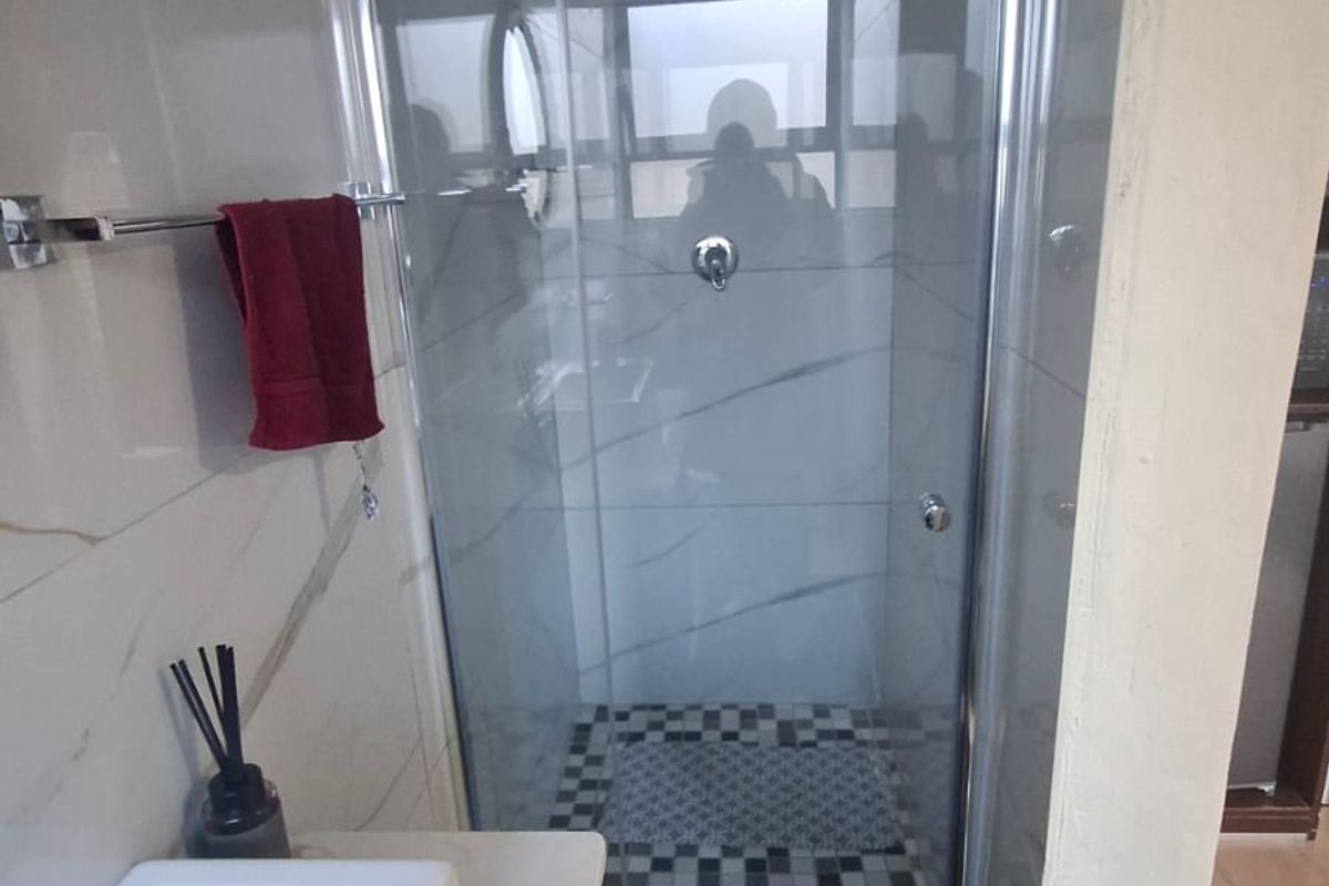 A modern bathroom featuring a glass-enclosed shower, marble-look wall tiling, and a sleek vanity basin.