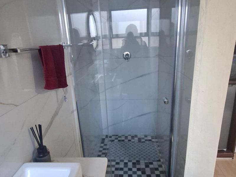 A modern bathroom featuring a glass-enclosed shower, marble-look wall tiling, and a sleek vanity basin.