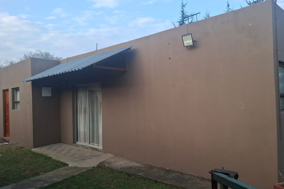 Rear exterior view of the house featuring a sliding glass door, metal awning, and paved walkway along the building perimeter.