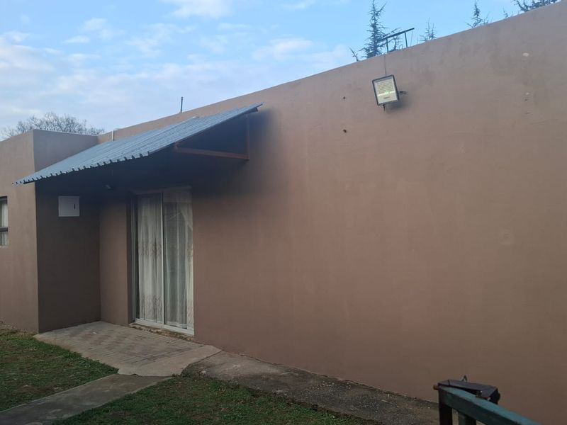 Rear exterior view of the house featuring a sliding glass door, metal awning, and paved walkway along the building perimeter.
