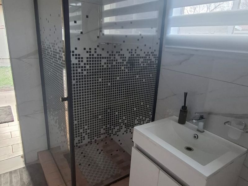Modern bathroom featuring a glass-enclosed shower, vanity cabinet with integrated basin, and contemporary wall and floor tiling.