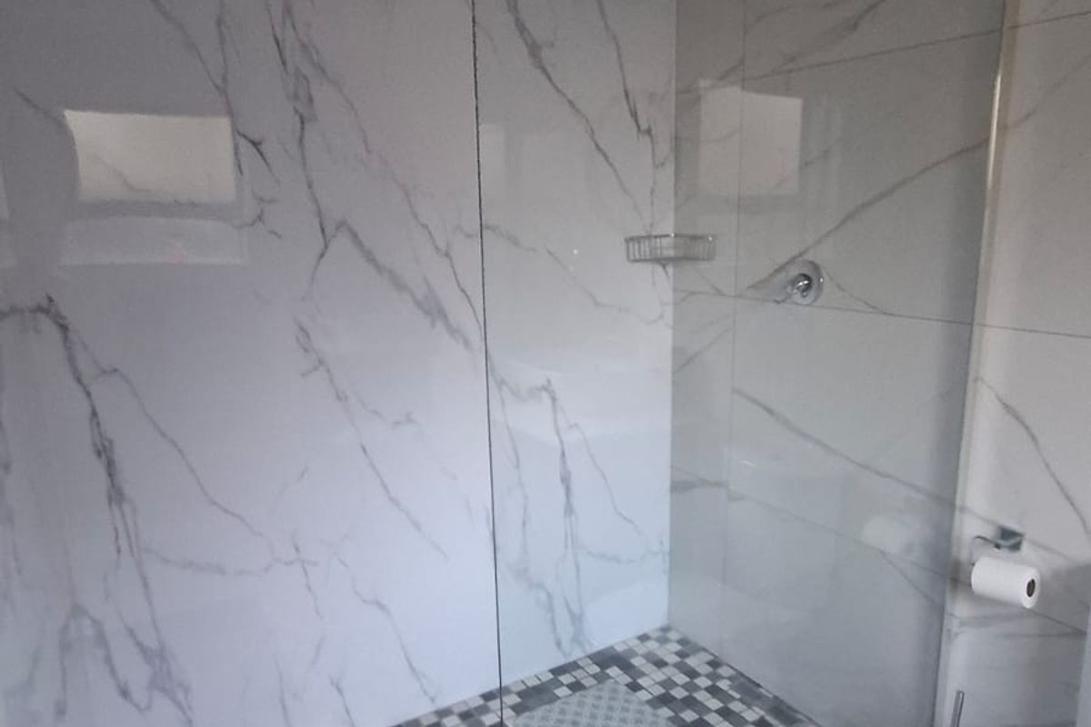 Modern bathroom featuring a walk-in shower with glass screen, marble-look wall tiling, and a mosaic-tiled shower floor.