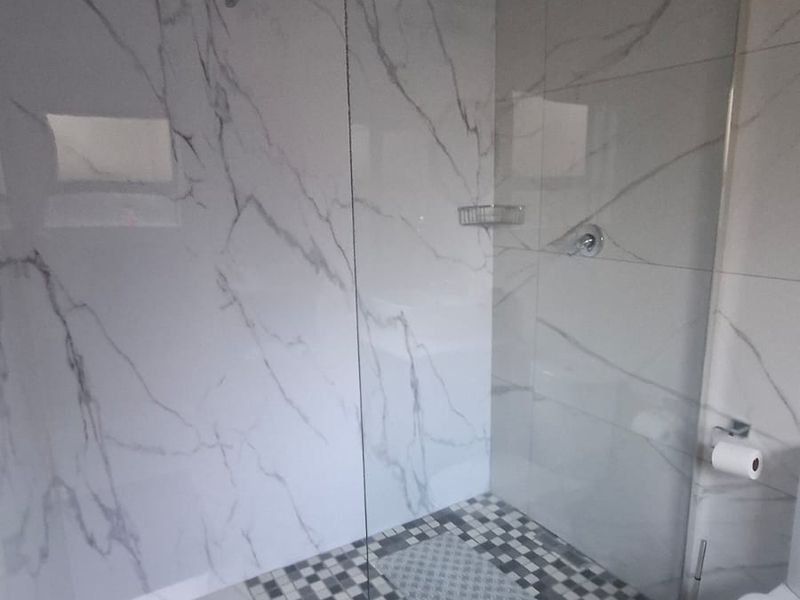 Modern bathroom featuring a walk-in shower with glass screen, marble-look wall tiling, and a mosaic-tiled shower floor.