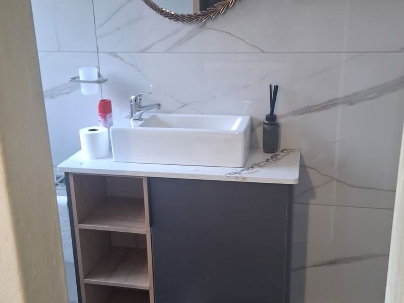 A compact bathroom featuring marble-look wall tiles, a modern vessel sink, and a vanity cabinet with open shelving.