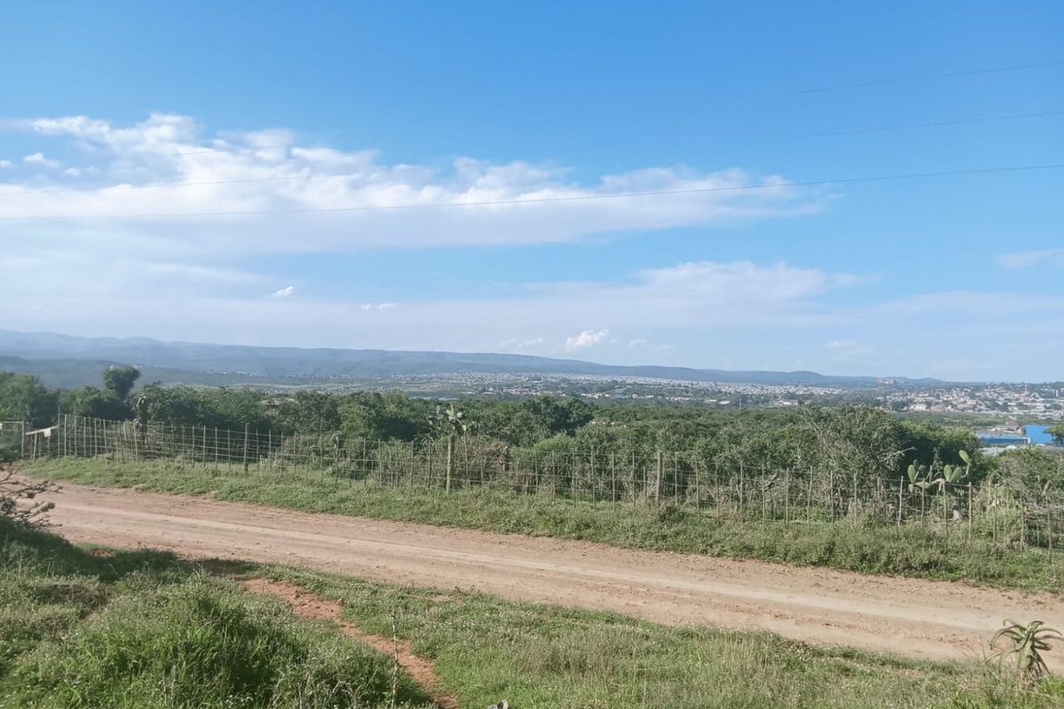 A scenic view overlooking the surrounding landscape and distant town, featuring a dirt access road and wire boundary fencing.