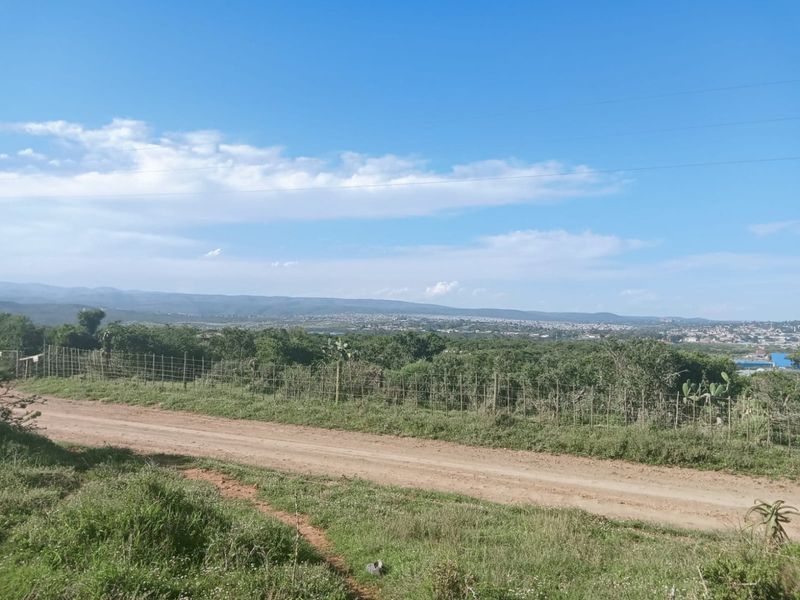 A scenic view overlooking the surrounding landscape and distant town, featuring a dirt access road and wire boundary fencing.