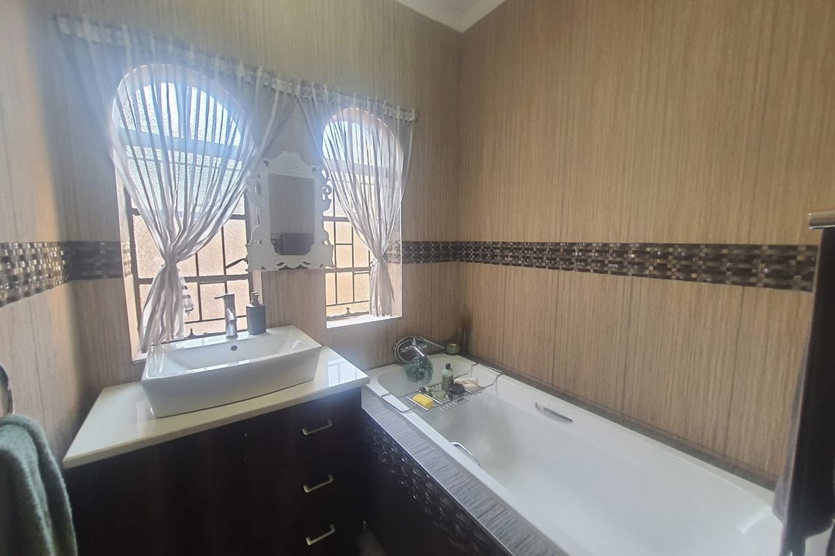 A bathroom featuring a built-in bathtub, a modern vessel sink vanity, and decorative tiled wall accents under arched windows.