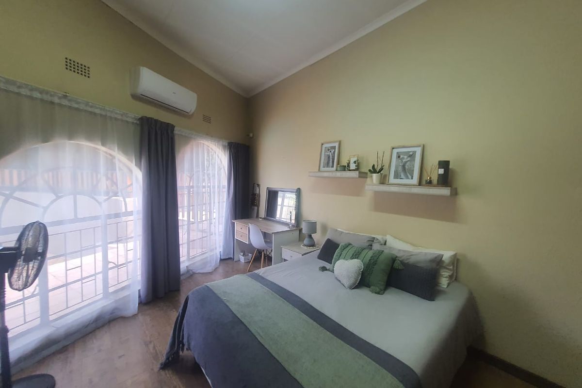 A bedroom featuring arched windows with security bars, laminate flooring, and a wall-mounted air conditioning unit.