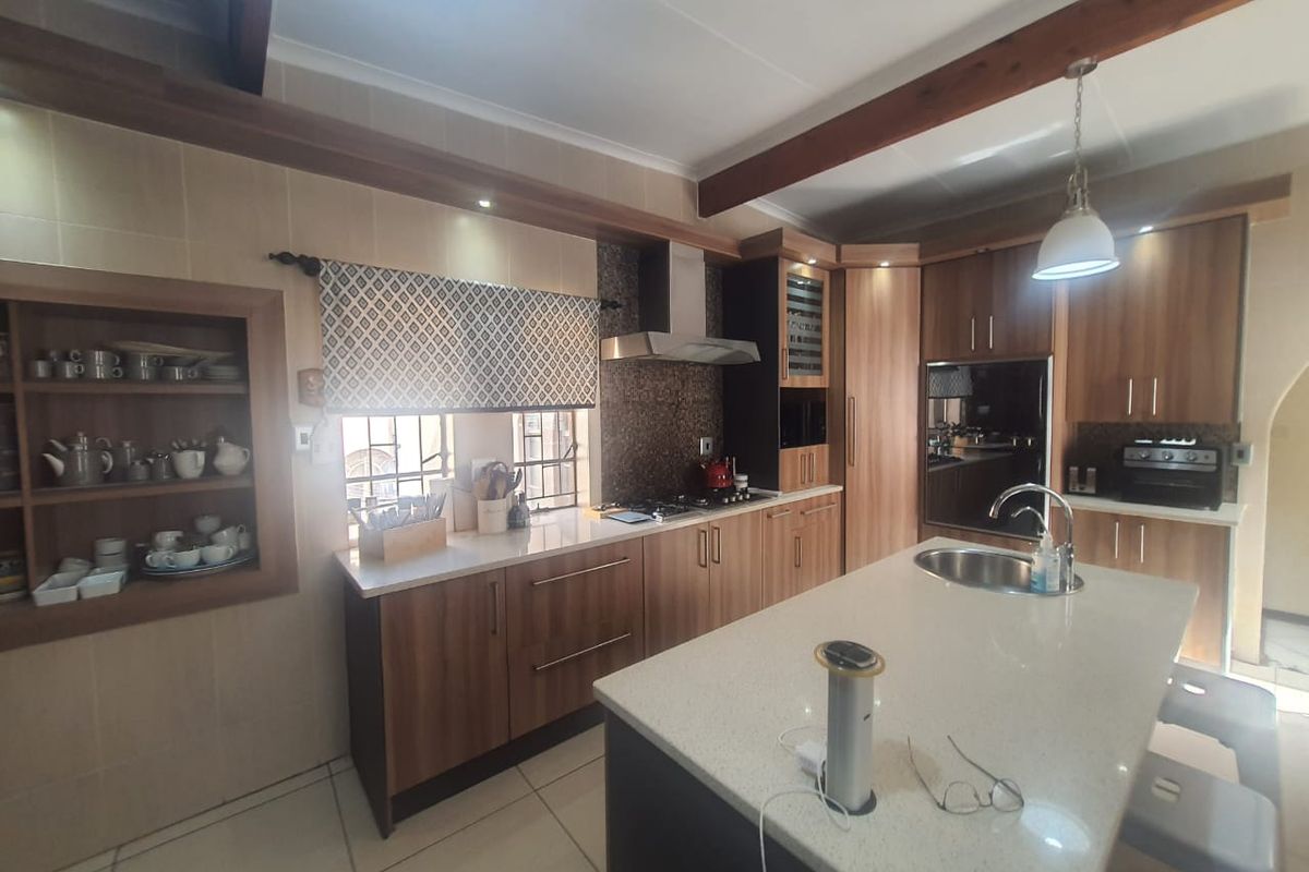 Modern kitchen featuring wood-finish cabinetry, stone countertops, a central island with a prep sink, and built-in stainless steel appliances.