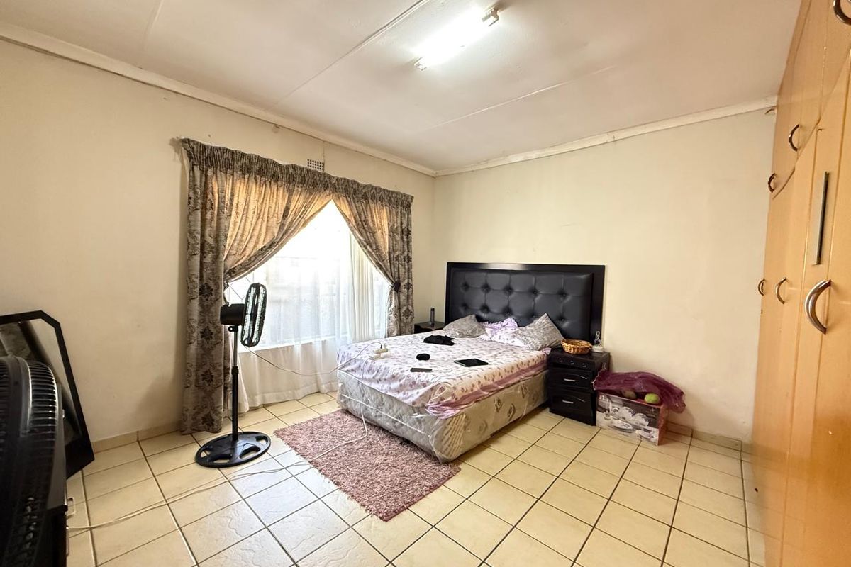 A functional bedroom featuring tiled flooring, built-in wooden cabinetry, and a large window with curtain tracks.